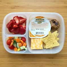 a plastic container filled with fruit and veggies on top of a wooden table