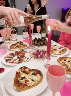 a woman pours wine into a glass at a table filled with pizza and appetizers