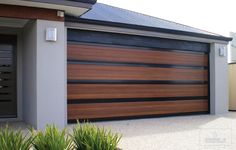 a house with a large wooden garage door in front of it and two plants on the sidewalk