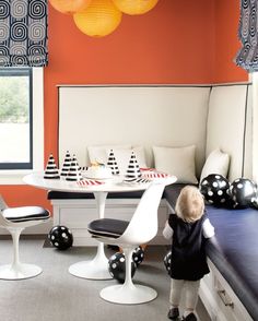 a little boy standing in front of a table with chairs and balloons hanging from the ceiling