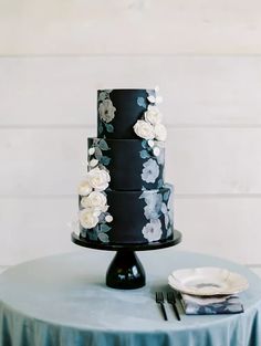 a black and white wedding cake with flowers on the top is sitting on a blue tablecloth