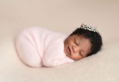 a baby is wearing a tiara and sleeping on a white blanket with her eyes closed