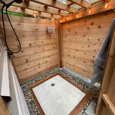 a wooden shower stall with lights on the ceiling and rocks in the ground below it