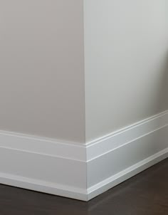 an orange cat sitting on the floor next to a white wall and wooden flooring