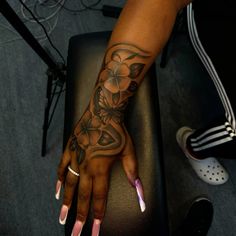 a woman's hand with flowers on it and white fingernails, sitting in front of a black chair