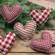 four red and white plaid heart ornaments sitting on top of a wooden table next to pine branches