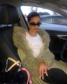 a woman sitting in the back seat of a car wearing sunglasses and a furry coat