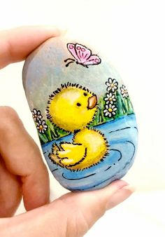 a hand holding a painted rock with a yellow rubber ducky on it's side