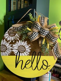 a wooden sign with the word hello painted on it and daisies in front of a green wall