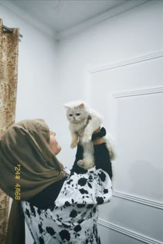 a woman holding a white cat in her arms while wearing a brown shawl over her head