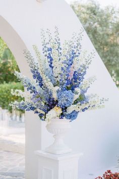 a white vase filled with blue and white flowers sitting on top of a stone slab