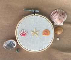 some seashells are sitting on a table next to a cross - stitch hoop