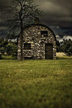 an old stone building with a tree in the foreground and dark clouds above it