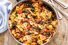 a pot filled with pasta and meat on top of a wooden table next to silverware