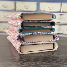 four books are stacked on top of each other in front of a dresser with drawers