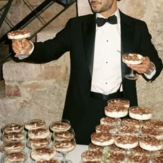 a man in a tuxedo is holding up some desserts and wine glasses