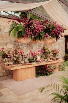 a wooden table topped with potted plants under a white cloth covered roof next to a stone wall