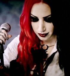 a woman with red hair and black makeup holding a microphone in front of her face