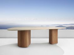 an oval table on top of a white wall with mountains in the background and blue sky