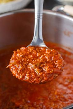 a ladle full of tomato sauce being held by a metal spoon with a piece of meat in it