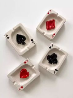 four playing cards with red and black hearts in them on a white surface, one is empty