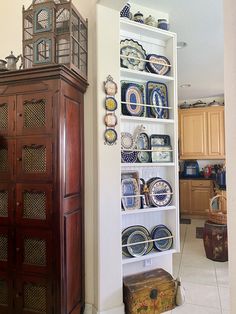 an old china cabinet with plates on it and a wooden chest in the corner next to it