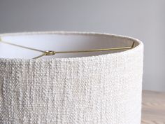 a white lamp shade on a table with a gold metal hook attached to it's side