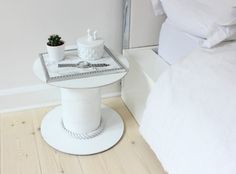 a small white table with a potted plant on it next to a mirror and bed