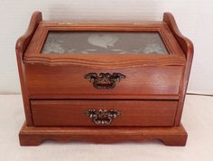 a small wooden box with glass top and drawer on the bottom, sitting on a white surface