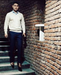 a man is standing on the steps in front of a brick wall and wearing a sweater