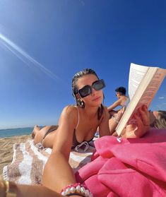 a woman laying on the beach reading a book