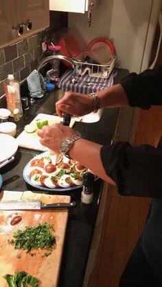 two people preparing food in a kitchen on top of a wooden cutting board with knifes