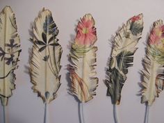 five feathers are lined up in a row on a white wall, one has pink flowers and the other is green leaves