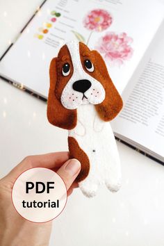 a hand holding up a stuffed dog on top of a white table next to an open book