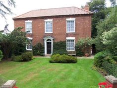 a large brick house surrounded by lush green grass and trees with red flowers in the front yard