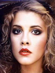 a close up of a woman with curly hair and blue eyeshadow wearing a black hat