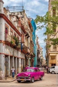 an old pink car is parked on the side of the road in front of some buildings