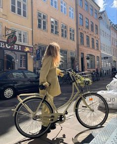 a woman is standing next to her bike on the sidewalk in front of some buildings