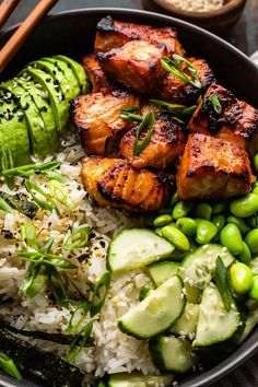 a bowl filled with rice, cucumber and meat next to chopsticks