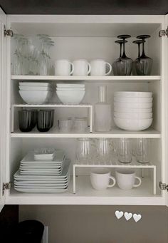 white dishes and cups are stacked on the shelves in this kitchen, which is organized with glassware