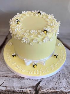 a yellow cake with white flowers and bees on it sitting on top of a wooden table