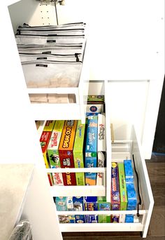 an open drawer in a white cabinet filled with lots of books and other items on top of it