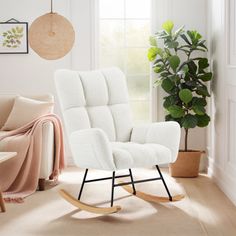 a white rocking chair sitting in a living room next to a potted green plant