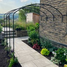 an outdoor garden with lots of plants and flowers in the area next to a brick building