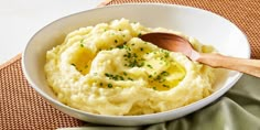 mashed potatoes in a white bowl with a wooden spoon on a tablecloth next to a green napkin