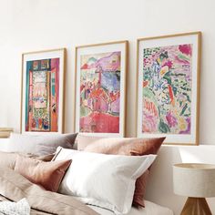 three paintings hang on the wall above a bed with white sheets and beige linens