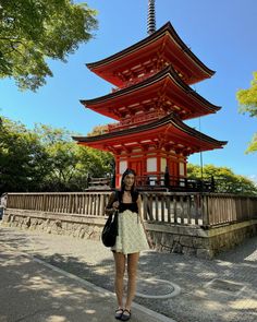 a woman standing in front of a tall red pagoda