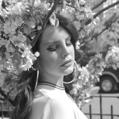 a woman standing under a tree with flowers on it's head and wearing large hoop earrings