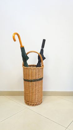 two umbrellas are placed in a basket on the floor next to a white wall