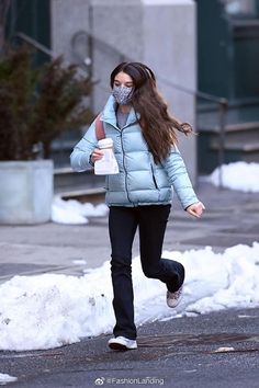 a woman walking down the street wearing a face mask and carrying a cup of coffee